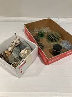 Two boxes, one containing assorted stones and shells, the other containing glass and metal flower frogs.