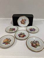 Six fruit plates displayed on white surface with black box in background. Five round 7 inch Bavaria plates showing different fruit paintings with gold rims.