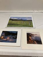 Three landscape photos displayed on a white surface showing the Upstate New York field, Big Sur coast cliffs and ocean, and the winter scene with snow and village buildings.