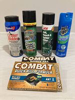 Full view of five pest control products including sprays and a bait box organized side by side on a white surface.