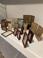 Photo showing 21 assorted picture frames displayed on a white surface, including folding and single frames in colors such as gold, black, red, brown, and silver.