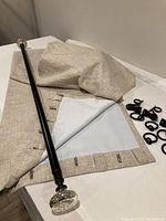 Beige lined drape panels folded showing the white lining and black adjustable curtain rod with mercury glass finial caps.