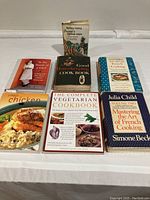 Photo of seven cookbooks showing titles and covers, including the Julia Child two-volume set and other cookbooks.