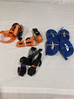 Overall lot image showing all seven tie down straps in orange, black, and blue, laid on a white surface.