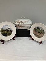 Set showing Ridgways English soup tureen flanked by two Currier and Ives reproduction plates on display stands