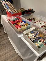 Photo showing rolls of wrapping paper including festive and plain kraft paper, large container with red, green, gold and patterned gift bows, box with assorted gift tags and some gift bags.