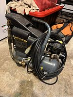 Side view of the black and gray 2 gallon air compressor showing handle, hose wrapped around, and metal fittings.