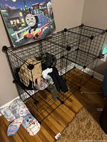 Black wire modular storage rack assembled in room corner containing clothing and bags, showing overall construction and dimensions.