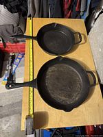 Two cast iron frying pans on a wooden surface, showing a 10-inch and a 12-inch pan with handles and helper handles.