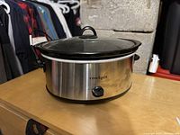 Photo of large oval Crock-Pot slow cooker with stainless steel body and glass lid, placed on a table.