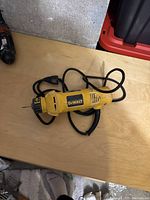Yellow Dewalt corded cutout tool with power cord on wooden surface, showing portability and general condition.