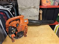 Photo showing the full orange leaf blower with black nozzle attachment and handle, placed on a wood surface.