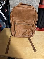 Front view of brown leather backpack with zippered front pocket.
