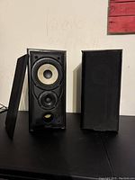 Pair of Mission bookshelf speakers with one grill removed showing woofer, tweeter, and bass reflex port.