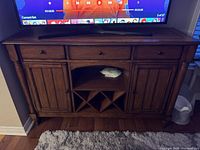 Front view of the real wood credenza with TV on top, showing full piece with drawers, cabinets, and wine rack space.