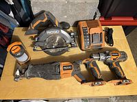 View of all tools laid out: circular saw, reciprocating saw, cordless drill, battery charger, portable LED work light, and carrying bag.