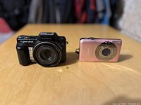 Both Sony Cyber-shot DSC-HX1 and pink Canon PowerShot cameras front view on table