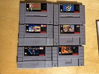Top-down photo of six Super Nintendo game cartridges arranged in two rows of three, showing labels for classic games.