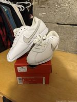 Pair of white Nike sneakers displayed on original Nike shoe box with visible size label T10770A in size 5.5.