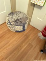 Side view of a blue round ottoman with white and light blue patterned fabric on a wooden floor near doors.