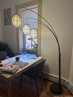 Full view of the arc floor lamp showing three hanging lantern-style lampshades over a desk.