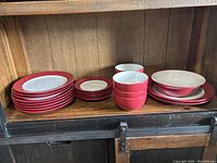 Overall view of Pfaltzgraff Harmony Red dinnerware set arranged on a wooden shelf, showing dinner plates, smaller plates, bowls, and serving plates.