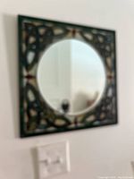 Blurry front view of the square hanging mirror featuring the circular mirror center and decorative green glass frame with red accents.