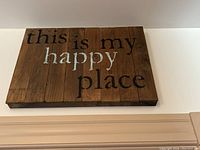 Wooden wall art panel with text 'this is my happy place' on rustic wooden slats.