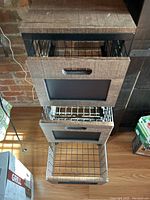 Front and open drawer view of kitchen storage holder showing wood fronts with chalkboard panels and wire mesh baskets.