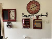 Red kitchen wall items mounted on white wall including clock, message board, plastic bag holder, note board, and metal sign.