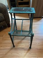 Side view showing turquoise metal frame with wear and chipped paint, wire mesh compartments for magazines underneath flat top.