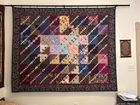 Front view of the handmade patchwork quilt hung on the black metal hanging rod on a white wall