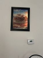 Framed artwork of tree with autumn foliage hanging on wall, showing warm color palette and black frame.