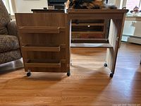 Wooden sewing table unfolded with three shelves on left side and caster wheels underneath.