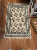 Photo of a small rectangular rug with cream background and blue floral designs, fringed edges visible