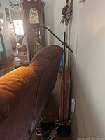 Black adjustable height spot lamp behind a sofa with visible weighted round base and cord.