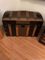 Front angled photo of vintage steamer chest showing curved top with leather straps and metal clasps.