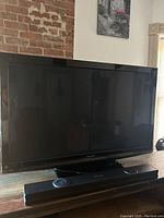 Front view of the Panasonic 50-inch TV with screen off and sound bar positioned in front of it on table.