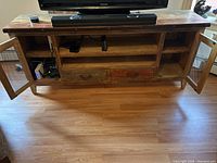 Front view of wooden TV stand with open shelves, drawers, and side meshed door cabinets, showing interior storage space