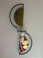 Pair of decorative wall sconces with metal frames, embossed leaf half-circle panels in red and green, each with a clear glass votive candle holder, mounted on white wall.