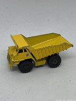 Side view of yellow Hot Wheels dump truck toy showing the dump bed and six wheels.