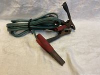 Jumper cables coiled, showing metal clamps with red and black insulated grips on white cloth background.