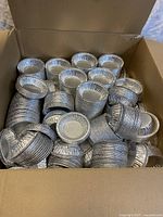 Open box full of small round disposable aluminum tart trays stacked inside.