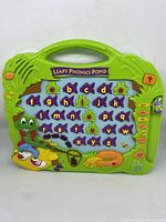 Front view of Leap's Phonics Pond phonics toy showing green plastic handle top, colorful purple fish alphabet letters, frog characters, and pond theme