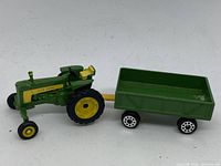 Miniature John Deere toy tractor attached to a green trailer with four wheels
