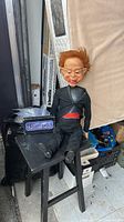 Large vintage ventriloquist doll seated on a small black stool with the Nightmare VHS tapes beside it.