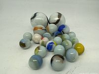 23 vintage opaque white glass marbles with colored swirl patterns arranged on a flat surface.