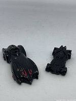 Photo showing both Batman Hot Wheels cars, classic Batmobile and modern bat-shaped vehicle, side by side on white background