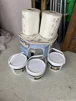 Photo shows two large rolls of protective stick foam on top of a box and three white plastic pails placed on the floor.