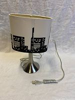 Front and side views of the skyline cityscape table lamp showing the shade and metal base with power cord.